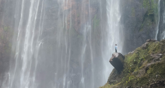 Person standing on a rock beside a tall waterfall